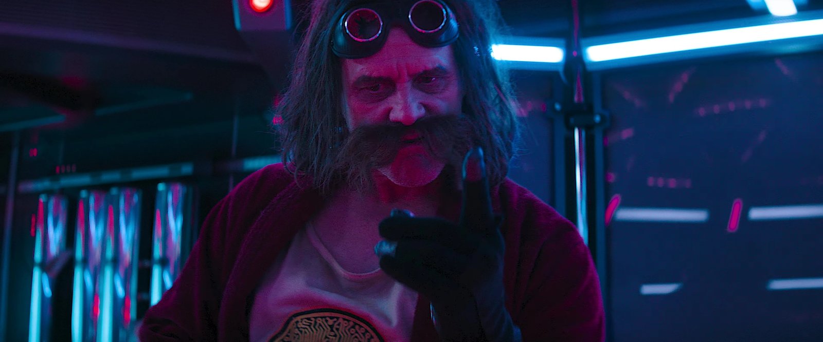 Sonic the Hedgehog 3 film still: Jim Carrey as Dr. Robotnik, goggles up, huge mustache, red jacket, pointing right at the camera in his neon-lit lab